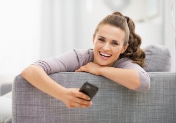Happy young woman with mobile phone sitting on sofa