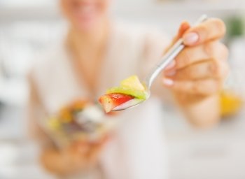 Closeup on young woman giving spoon with salad