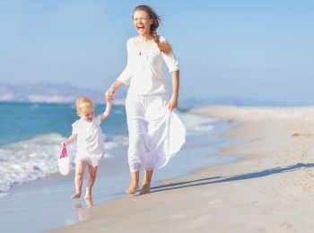 Happy mother and baby running along sea coast