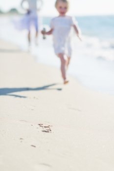 Closeup on sand and mother and baby running along sea shore