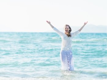 Smiling young woman standing in sea and sprinkling water