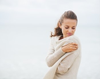 Young woman wrapping in sweater on coldly beach