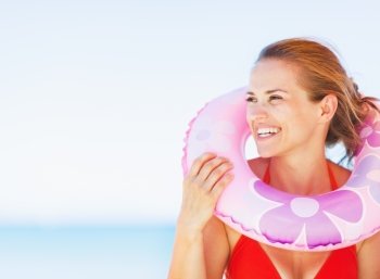 Portrait of smiling young woman on beach with swim ring looking on copy space
