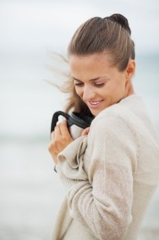 Happy young woman in sweater on beach with cup of hot beverage