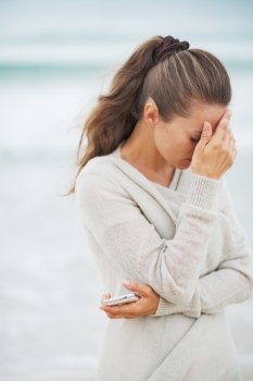 Stressed young woman in sweater on beach with mobile phone