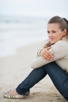 Young woman in sweater sitting on lonely beach looking into distance