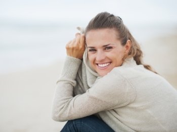Portrait of happy young woman in sweater sitting on lonely beach