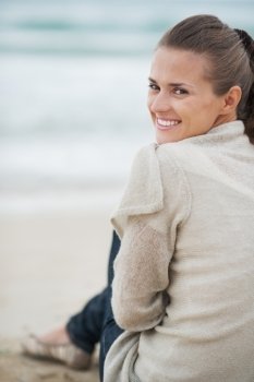 Smiling young woman in sweater sitting on lonely beach