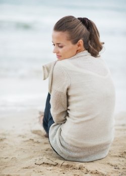Thoughtful young woman in sweater sitting on lonely beach
