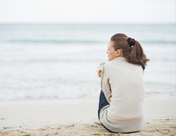 Young woman wrapping in sweater while sitting on lonely beach