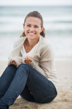 Happy young woman wrapping in sweater while sitting on lonely beach