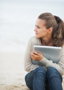 Young woman in sweater sitting on lonely beach and embracing laptop