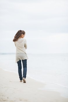 Thoughtful young woman in sweater walking on lonely beach . rear view