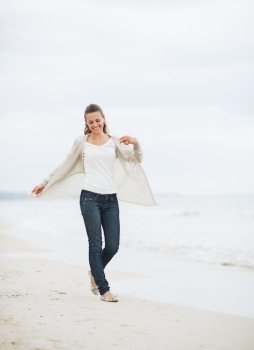 Smiling young woman in sweater walking on lonely beach