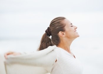 Happy young woman in sweater on lonely beach rejoicing