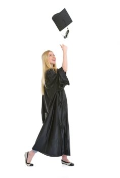 Full length portrait of happy young woman in graduation gown throwing cap up