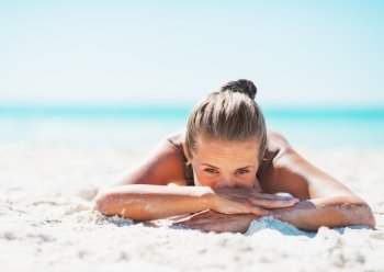 Young woman in swimsuit laying on sandy beach
