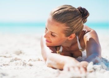 Relaxed young woman in swimsuit laying on sandy beach