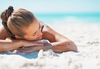 Happy young woman in swimsuit relaxing while laying on sandy beach