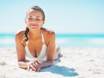 Happy young woman in swimsuit enjoying laying on sandy beach