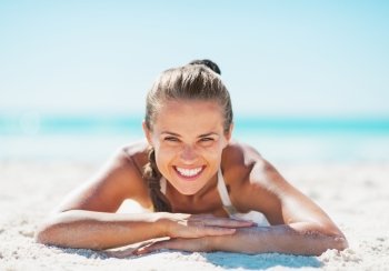 Portrait of smiling young woman in swimsuit laying on sandy beach