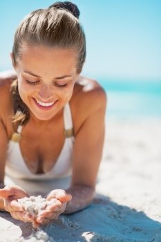 Happy young woman in swimsuit laying on beach and playing with sand