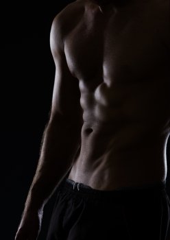 Closeup on muscular male torso with abdominal muscles on black