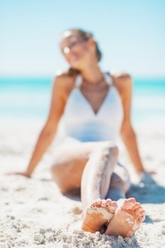 Closeup on legs of young woman in swimsuit sitting on beach