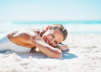 Happy young woman in swimsuit laying on sandy beach