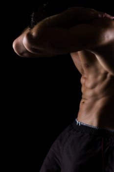 Strong muscular athlete showing abdominal muscles on black