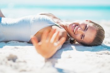 Smiling young woman in swimsuit laying on beach and greeting