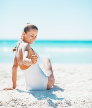 Closeup on smiling young woman in swimsuit sitting on beach and playing with sand