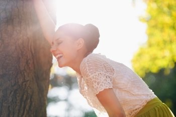 Laughing young woman lean against tree