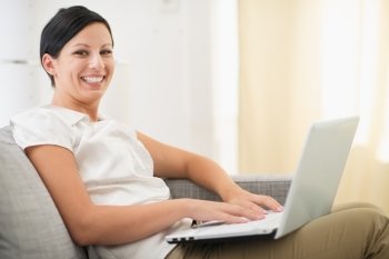 Smiling young woman surfing net on laptop in living room