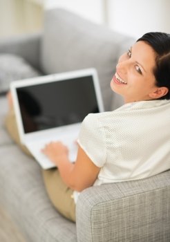 Smiling young woman laying on couch and using laptop