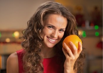 Portrait of smiling young housewife with orange in christmas decorated kitchen