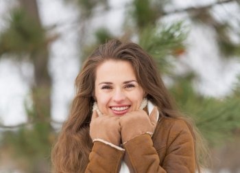 Portrait of happy young woman against fir-tree in winter outdoors