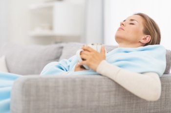 Ill woman with cup of hot beverage sitting on couch