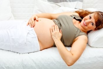 Smiling beautiful pregnant woman relaxing on sofa at home and  holding her tummy.
