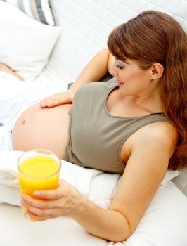 Beautiful pregnant female relaxing on sofa at home with glass of juice  in hand
