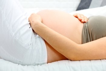 Pregnant woman lying on sofa at home and holding her belly. Close-up.
