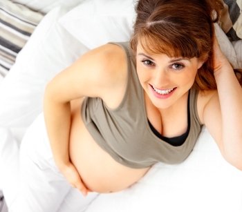 Smiling beautiful pregnant woman lying on couch at home and  holding her belly.
