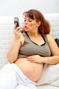 Smiling beautiful pregnant woman sitting on sofa at home and talking mobile phone.
