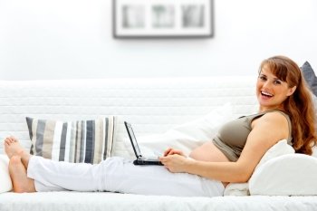 Smiling beautiful pregnant woman on sofa at home with the laptop and a  credit card.
