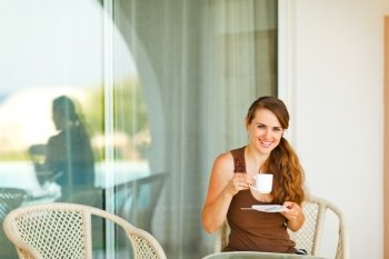 Smiling young woman sitting on terrace and drinking coffee
