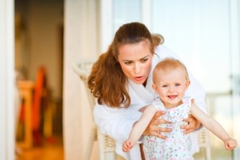 Young mother in bathrobe telling something to her adorable baby
