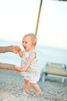 Happy baby on the beach trying to start walking with mothers help