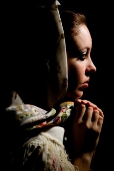 Portrait of young girl with old russian shawl on head on black background. 

