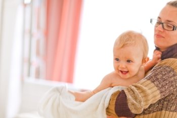 Cheerful baby on mamas arms looking in corner at home
