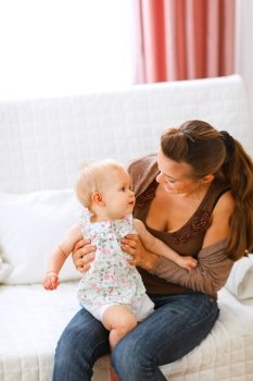 Adorable baby and young mom playing on couch at home
